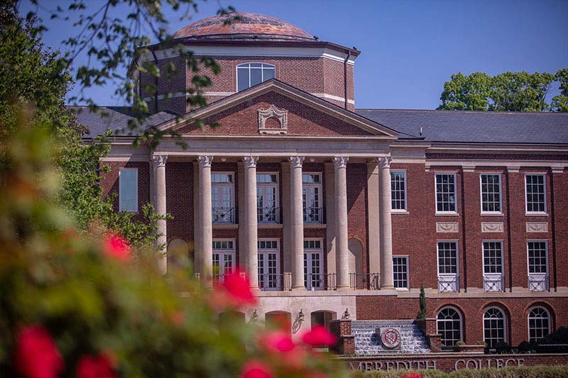 Image of Johnson Hall with a rosebush out of focus in left corner foreground.