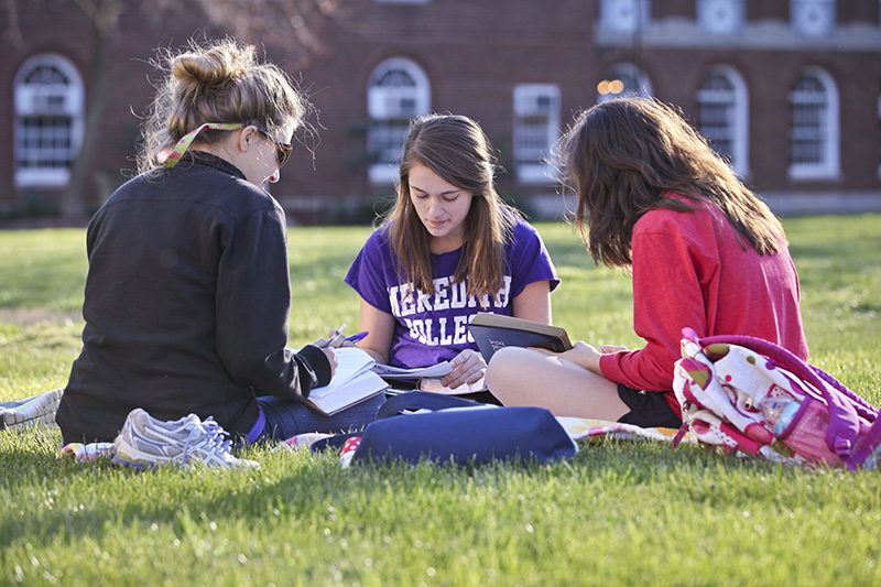 A group of three students sitting in a circle in the grass together.
