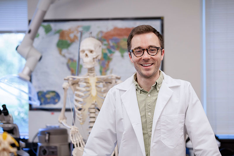 Ian Taylor in a lab coat and in front of a skeleton.