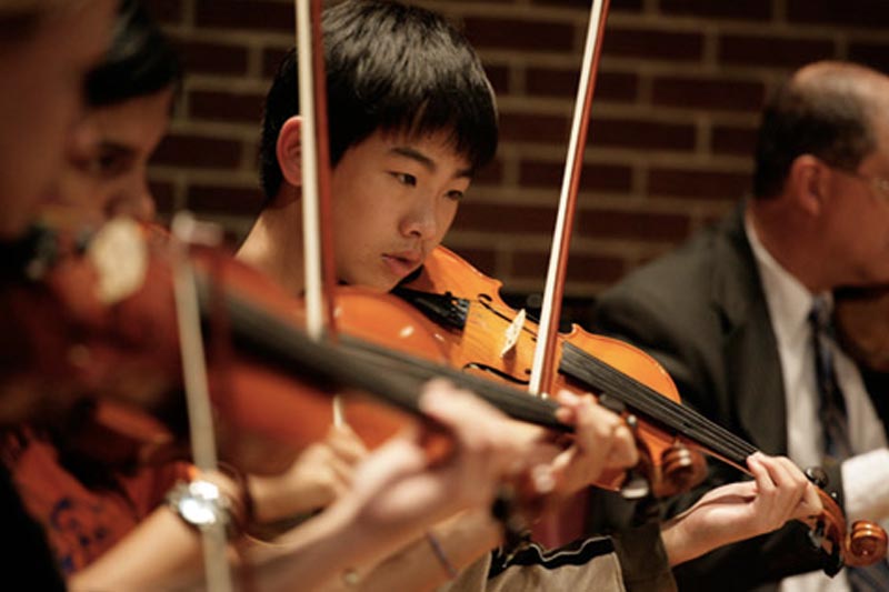 A young boy playing Violin around other artists.