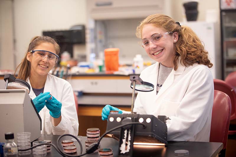 two students in lab coats smiling