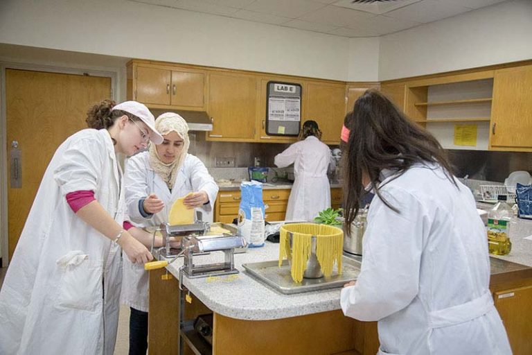 Image showing four students working in the food lab. They are making pasta in the image.