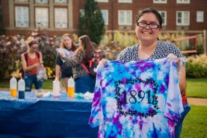 A student holding up a newly tie-dyed t-shirt that says 