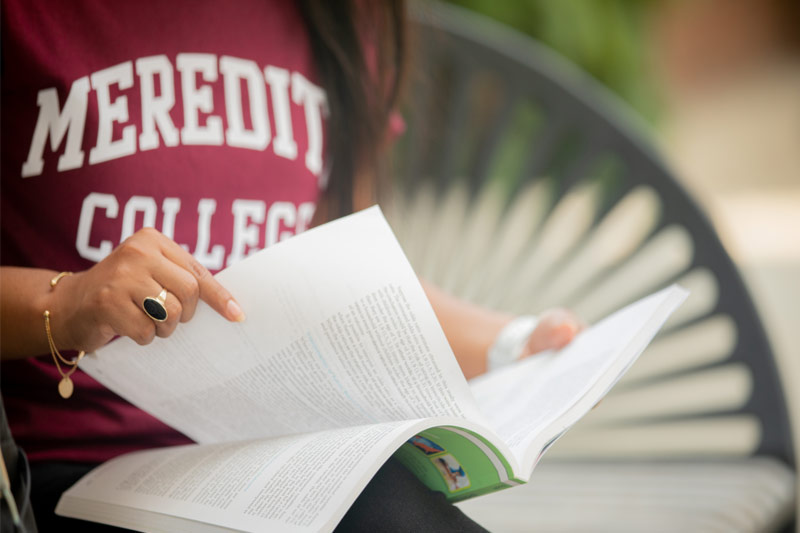 A student wearing a Meredith College sweatshirt looks through a document.
