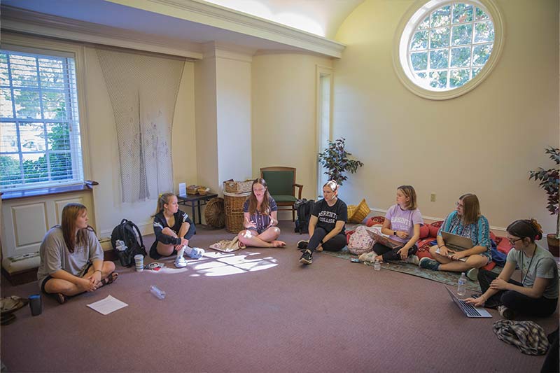 Seven students sitting on the floor in a semi-circle in a reading discussion group