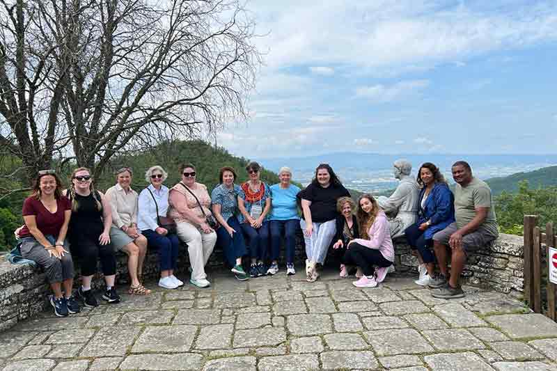 Members of the Spring 2023 Faculty Staff Italy Trip sit on a wall overlooking Italy.