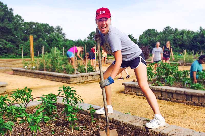 A student grins while shoveling in a community garden.