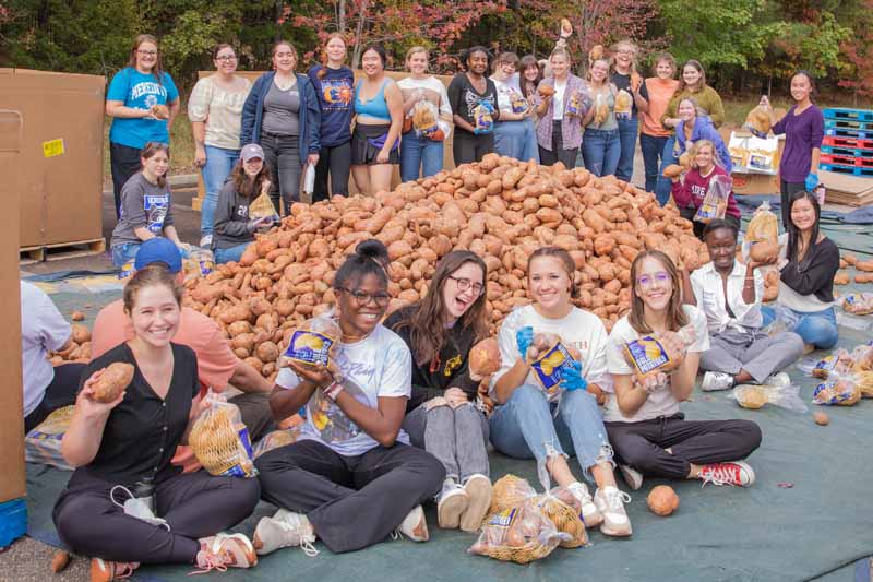 Students smile around a giant pile of yams for the yam jam.