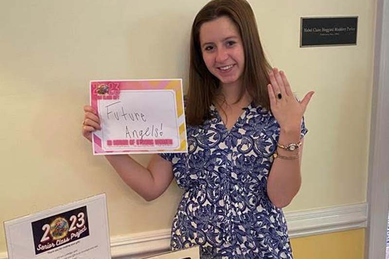 A woman showing off her Meredith ring while holding a sign that says Future Angels for the 2023 senior class project.