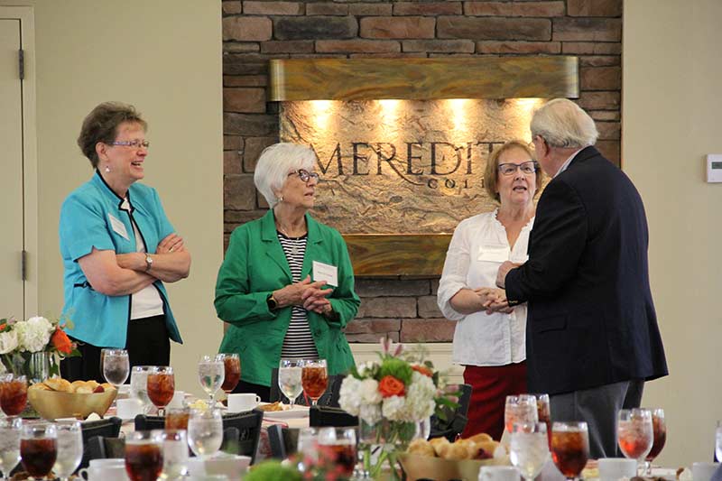 Four retired faculty and staff members at the 2023 luncheon with food and drinks set on tables in front.