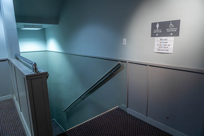 A stairwell with a sign that points down to the womens restroom and then right to the accessible bathroom.