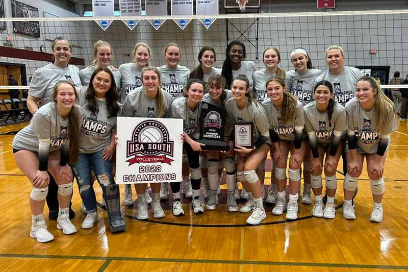 The Meredith Volleyball team smiles big with a trophy, plaque, and sign that say USA South Volleyball 2023 Champions.