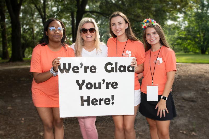 Three students and President Aimee Sapp hold a sign saying We're Glad You're Here as Meredith College welcomes the incoming class on Move-in Day 2024.